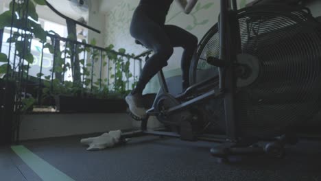 a low angle shot of a white female riding a stationary bike at a gym