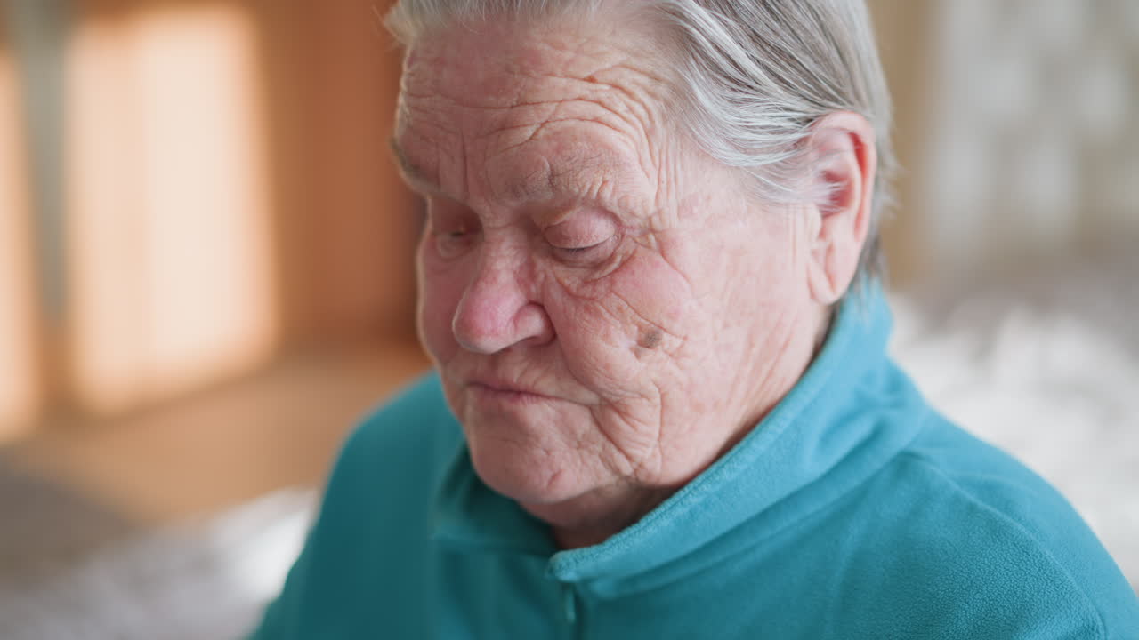 Lonely pensioner in green teal sweater carefully adjusts glasses. Close-up of wrinkled hands adjusting eyewear while sitting in well-lit room. Focus on elderly person's delicate movements and expressions