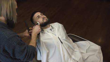 a barber uses an electric clipper to cut a client's hair or trim his beard in a barbershop