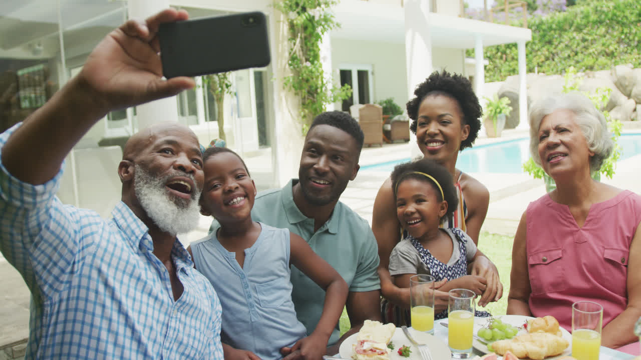 행복한 아프리카계 미국인 가족이 셀피를 찍고 정원에서 아침을 먹습니다.