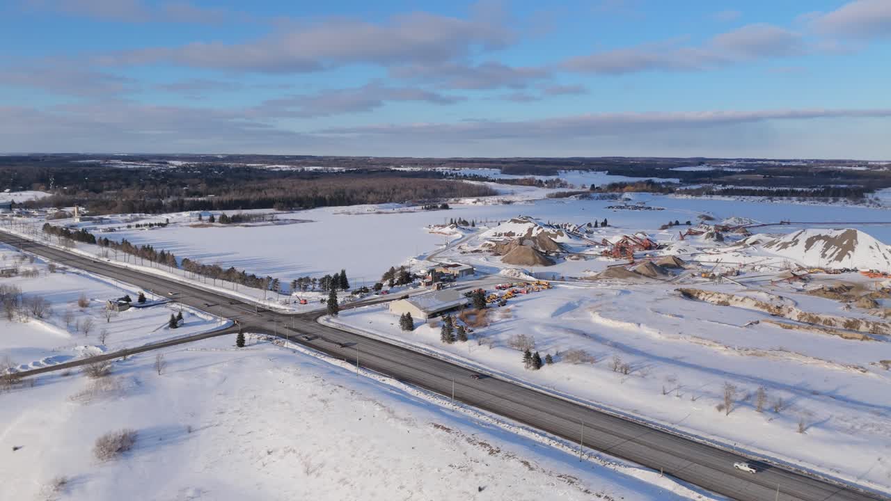 Luchtfoto met drone van bewegende voertuigen op Highway 10 nabij een sneeuwbedekte grindgroeve in Caledon Ontario, met een winterlandschap, open velden, een industrieel winningsgebied en landelijke omgeving.