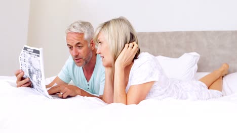 couple lying on bed reading newspaper together