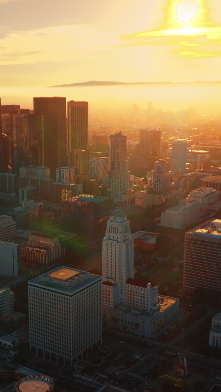 Wonderful panorama of contemporary Los Angeles at sunset. Hazy skyline in the bright light of sun rays at backdrop. Aerial view. Vertical video