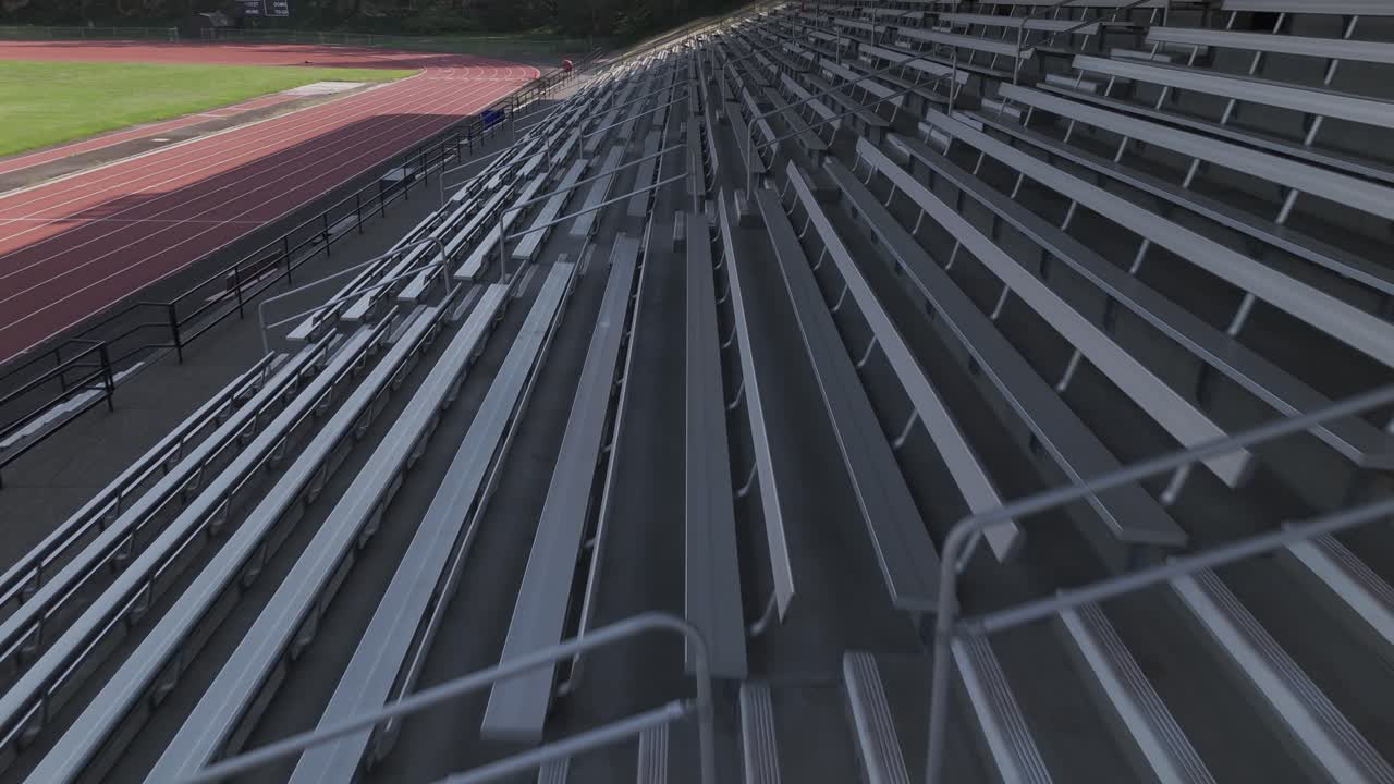 Drone shot fly over empty bleachers with running track in the background