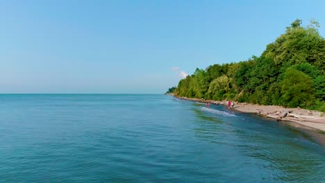 Aerial-footage-of-lake-coastline-with-people-playing-in-the-water-in-the-background