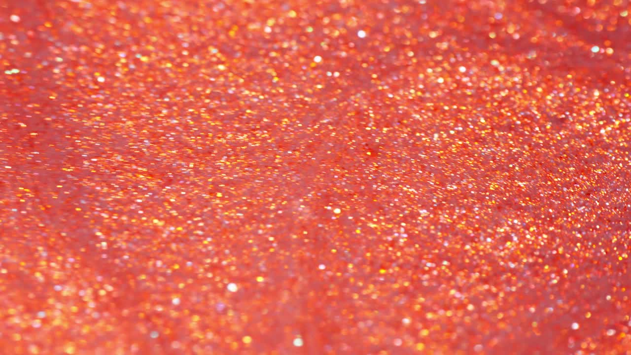 Mixing vibrant orange ink and glitter in a close-up macro shot creating an abstract scene