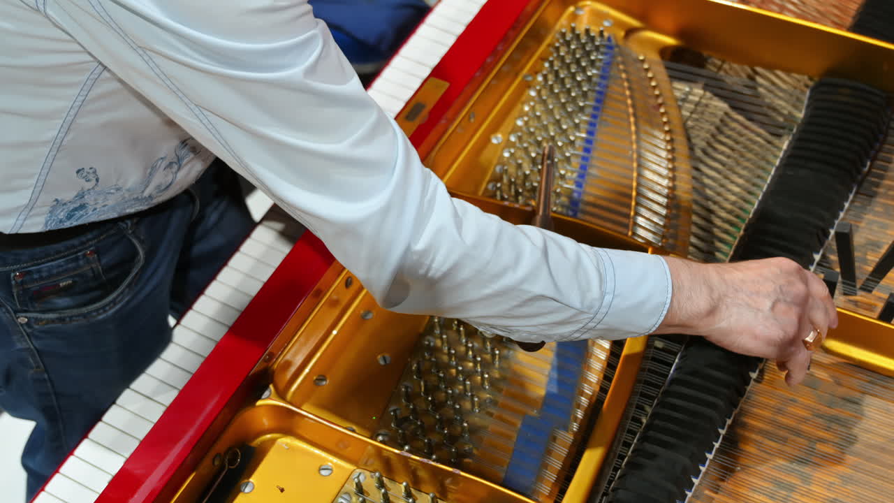 Primo piano di un uomo che sta riparando un pianoforte rosso
