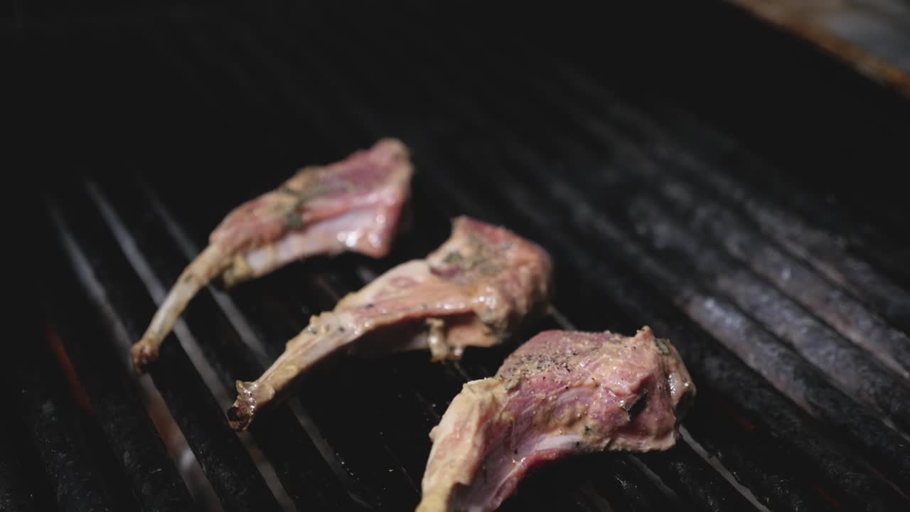 chuletas de cordero asadas en parrilla de barbacoa en llamas de cocina profesional levantando humo cocinando la carne cruda en parrilla de hierro fundido negro medio apretada panorámica hacia abajo constante cámara lenta
