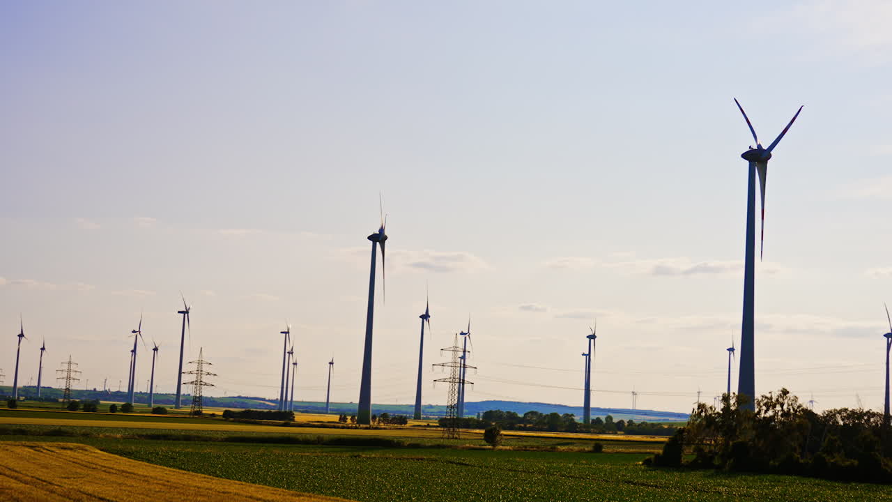 Wind turbines and power lines towers in the countryside. Low angle view at the wind farms generating green energy.