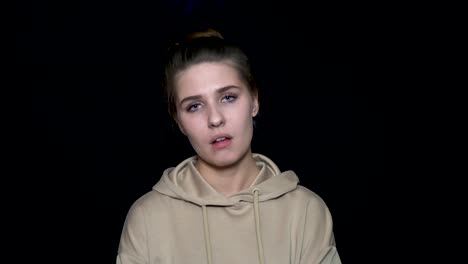 young woman wearing a light beige hoodie against a black background