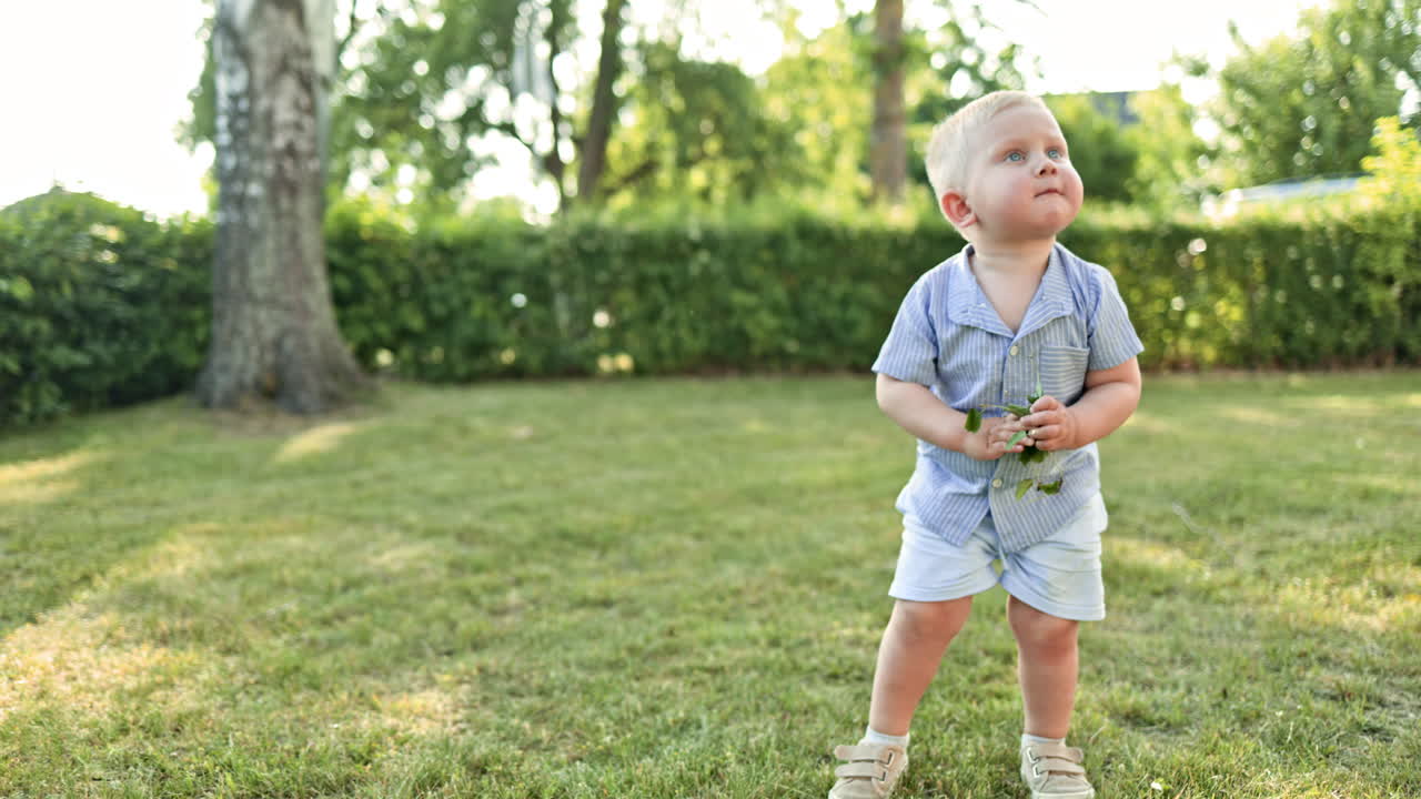 Toddler running on green grass. Active children's recreation. Smiling boy in shorts running and playing, having fun in the backyard on a sunny hot summer day. White boy playing hide and seek