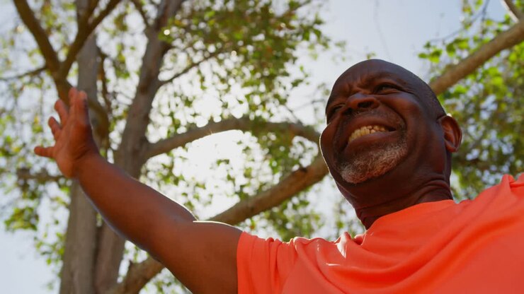 Inquadratura dal basso di un anziano afroamericano attivo che pratica yoga nel giardino di una residenza per anziani 4k