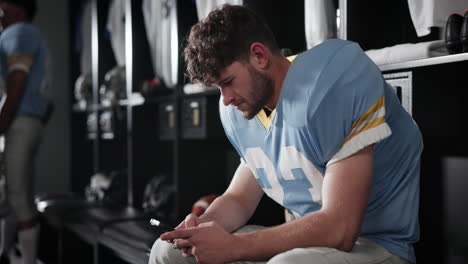 football player in locker room using mobile phone