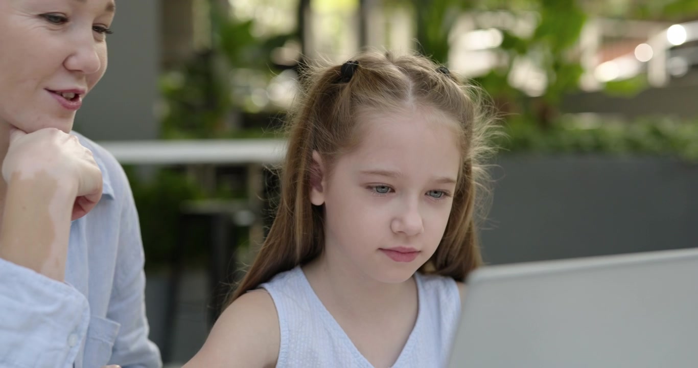 Donna che insegna a una giovane ragazza come usare un laptop all'aperto