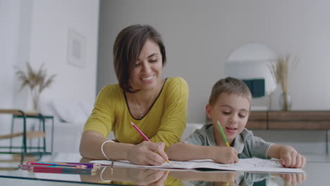 beautiful young mother in a warm sweater lying on the floor with my son drawing with markers on paper portraying his family. the child learns to draw