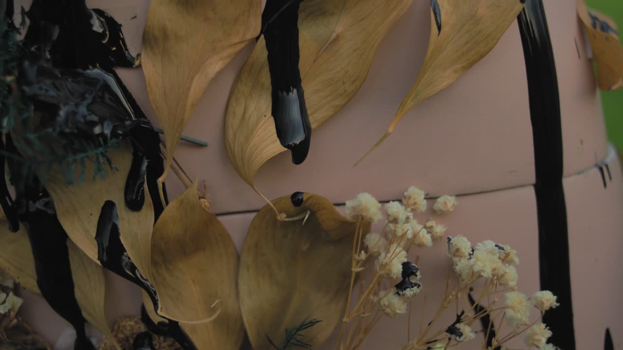 Dried Leaves and Flowers Arrangement on Pink Surface with Black Paint Drips