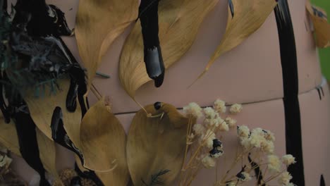 dried leaves and flowers arrangement on pink surface with black paint drips