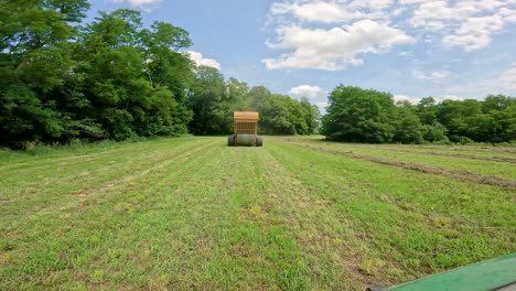 view from back of yellow hay baler ejecting a finished large round bale of hay in an alfalfa field