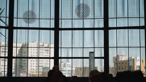 a modern building interior featuring large floor-to-ceiling windows with cityscape views and people moving in the foreground