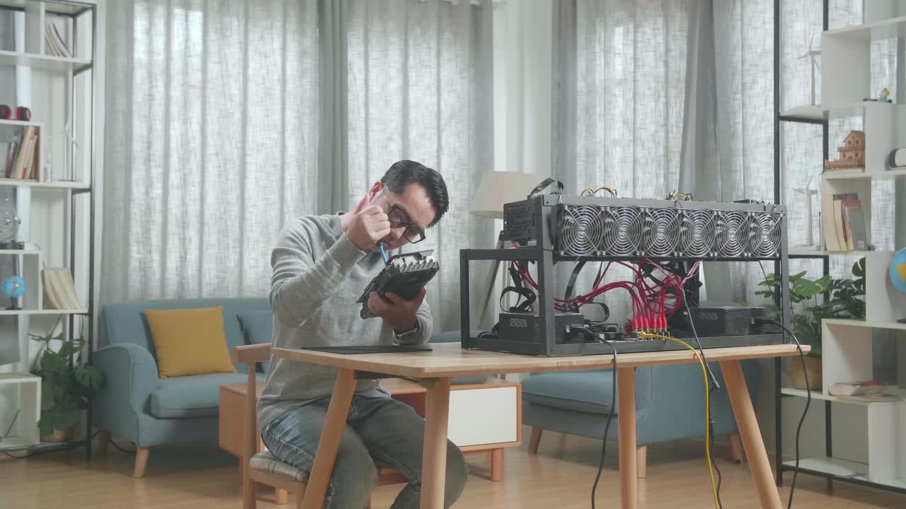 안경을 쓴 아시아인 남자가 암호화폐를 채굴하기 위해 그래픽 카드를 청소합니다.