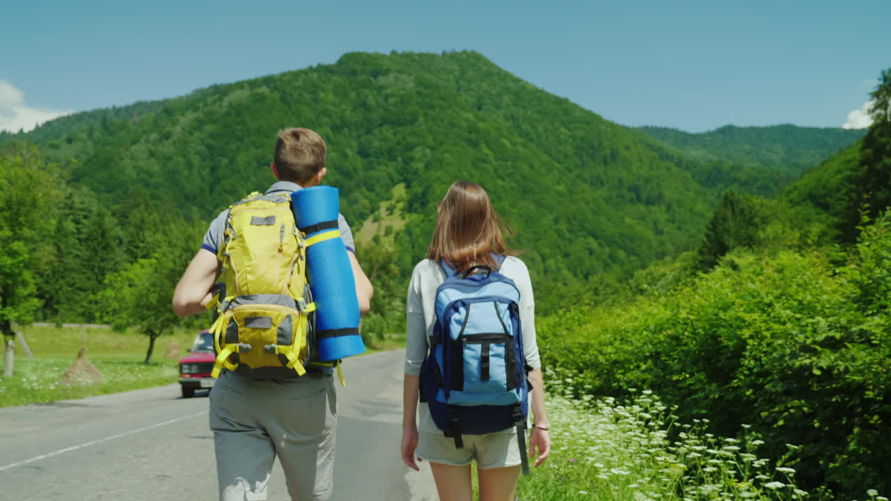 una joven pareja de turistas camina por el camino hacia hermosas montañas cubiertas de bosques forma activa de