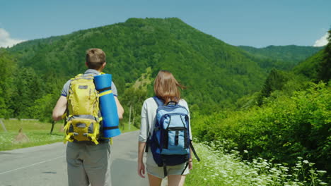 a young tourist couple walks along the road to beautiful mountains covered with forest active way of