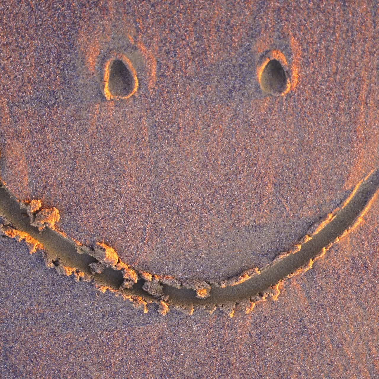 Drawing on wet sand. Handwritten smiley on a sandy sea beach is washed by the sea wave in summer. Top view.