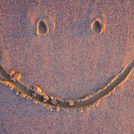 drawing on wet sand. handwritten smiley on a sandy sea beach is washed by the sea wave in summer. top view.