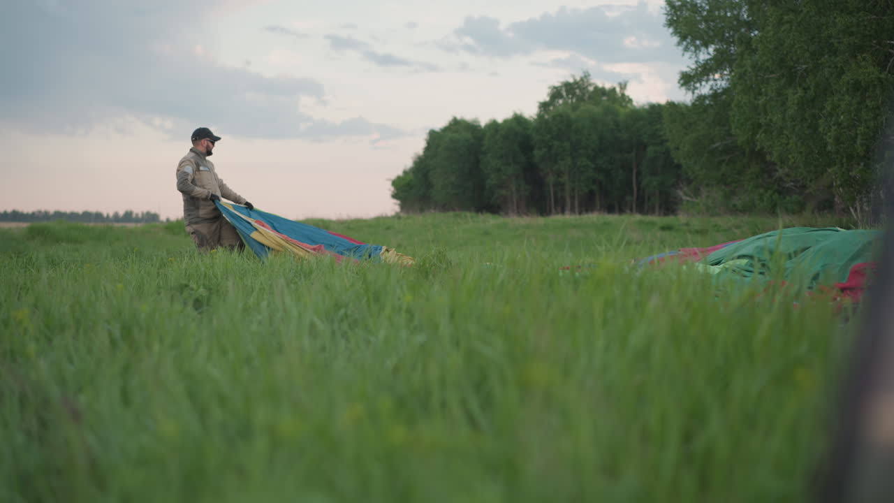 couple working together unfolding vivid balloon envelope on grassy field near forest edge during sunset prep for flight capturing teamwork excitement scenic outdoor atmosphere