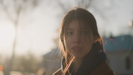 close-up shot of a girl walking with her hair partially covering her face, expressing a profound sense of grief. the soft backlighting from the sunset enhances the somber mood