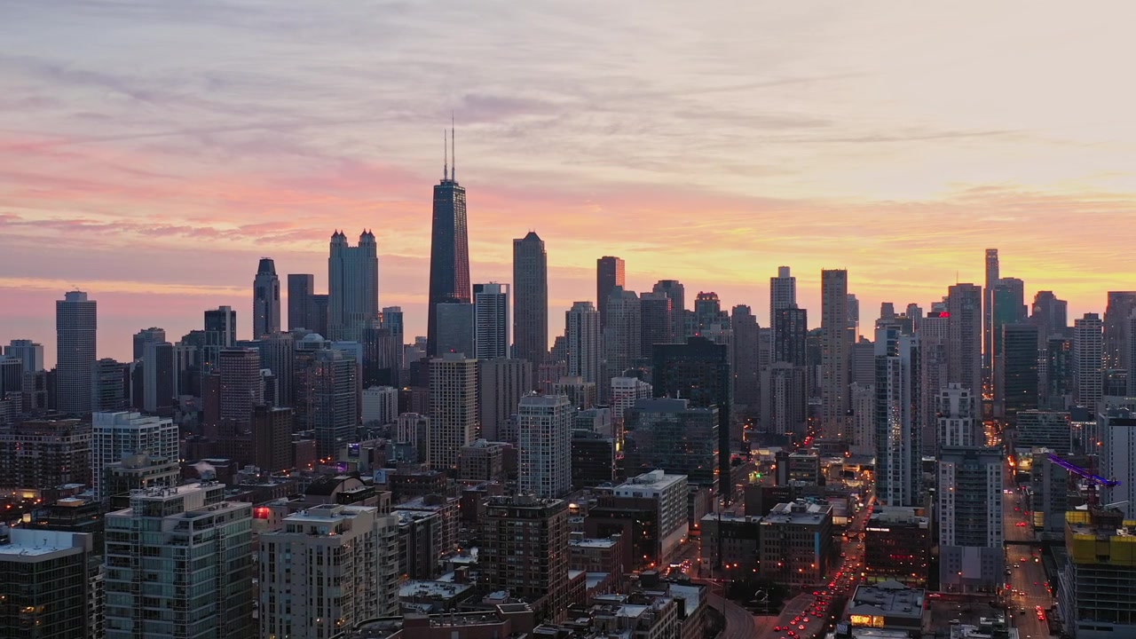 Ampie riprese aeree che dominano Chicago all'alba, mentre il denso skyline urbano si trova sotto strati di nuvole rosa, arancioni e dorate che brillano all'alba