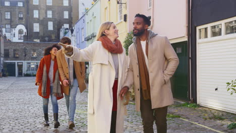 multi-cultural group of friends hugging as they walk along cobbled mews street on visit to city in autumn or winter - shot in slow motion