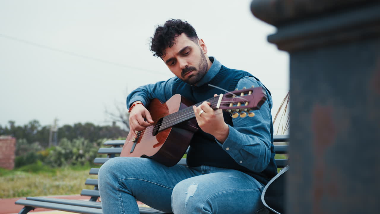 Man Relaxes on a Bench Playing the Guitar Outdoors