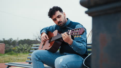 man relaxes on a bench playing the guitar outdoors