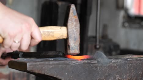 blacksmith stokes a coal fire and pounds a red hot peice of metal with a hammer