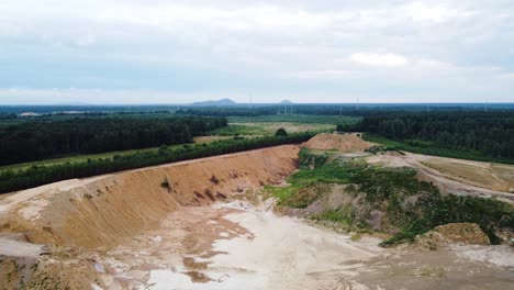 Massive-sand-quarry-surrounded-by-dense-green-forest,-aerial-view