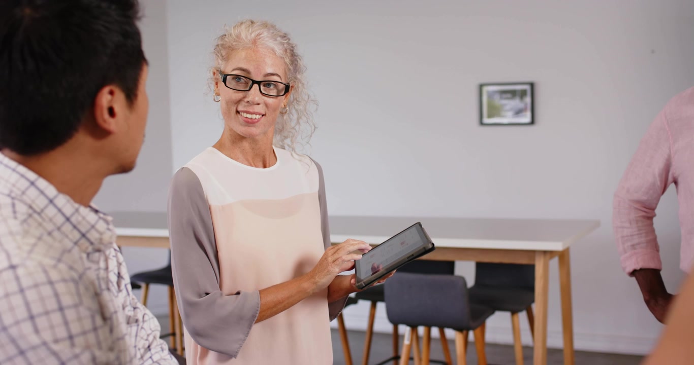 Presentatore che tocca il tablet e spiega, con un "SU" magenta che appare, etichette che si impilano e un collega che si sposta.