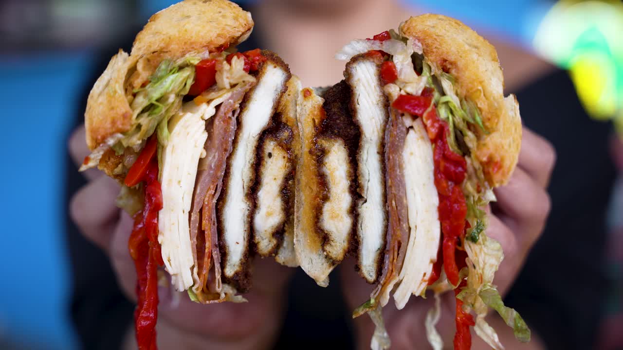 Zooming in close up in 4K of a chicken cutlet sandwich with roasted peppers that's just been cut in half and opened to reveal the filling by hands with a perfect manicure