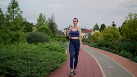 woman walking in park with yoga mat