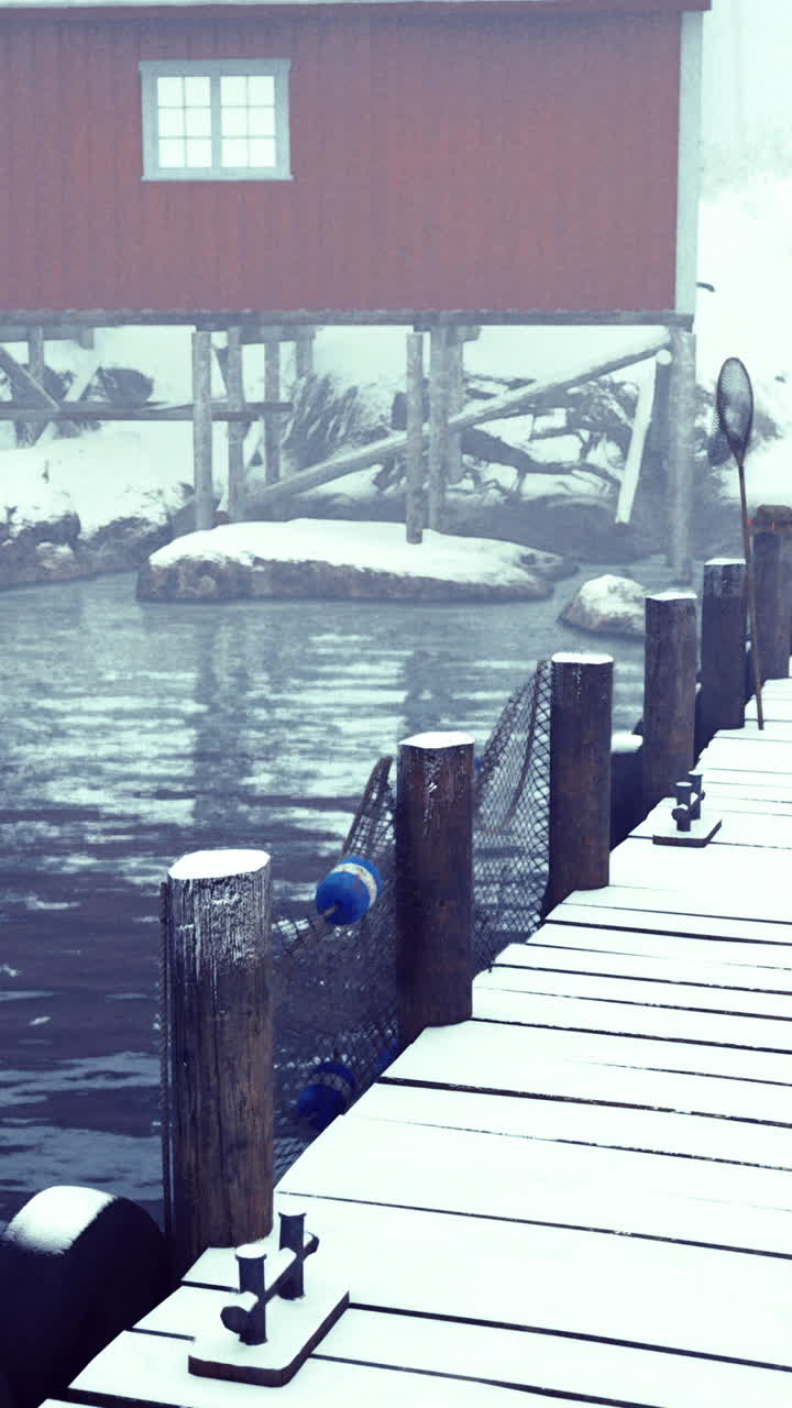 Snow covered dock with a red cabin near calm water during winter