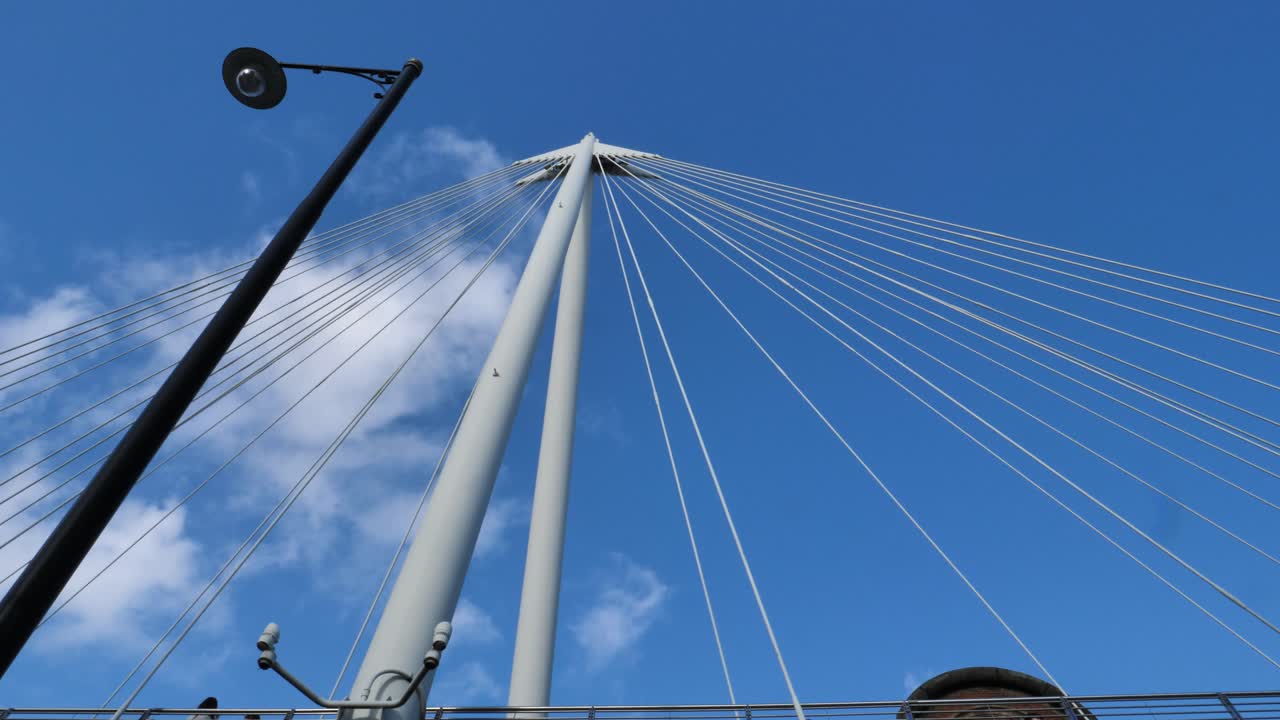 The structure of a modern bridge over the river Thames in London (UK) creates a geometry with a cloud on the sky beyond. At the end we see tourists walking over and under the bridge.