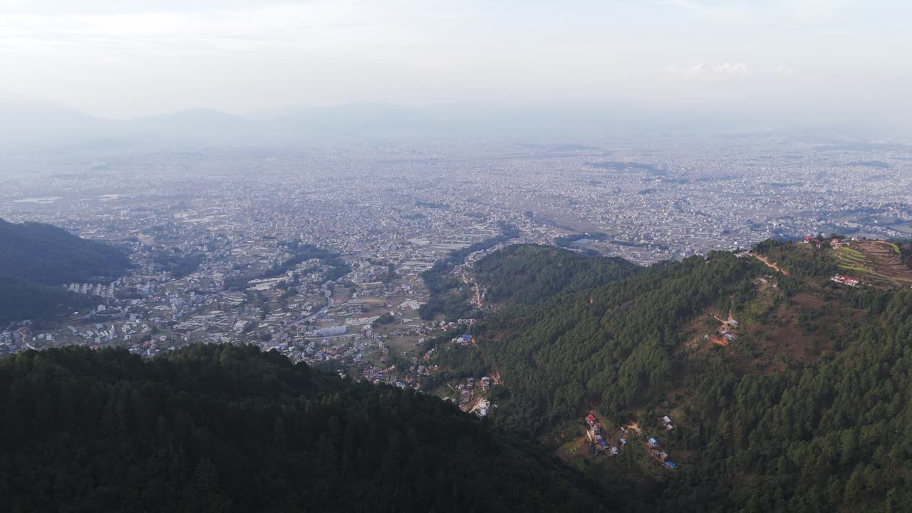 Drone view of Kathmandu Valley revealing its dense urban layout, surrounding green hills, and distant Himalayan horizon, capturing the unique blend of culture, terrain, and city life in Nepal