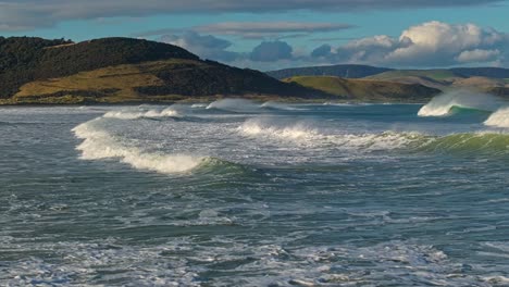 Aerial-tracking-sideview-follows-waves-crash-as-mist-flies-off-top,-New-Zealand