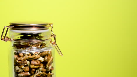 detalle de un tarro de albañil hermético que gira con nueces de pacana sobre un fondo amarillo neón