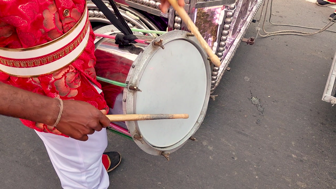 Hands playing drum on street during festival or parade, rhythmic motion, cultural percussion, natural sunlight highlights, energetic outdoor performance