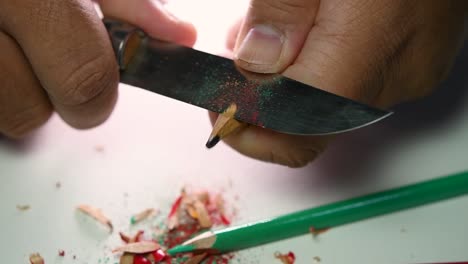 imágenes de manos afilando lentamente un lápiz y algunos lápices de colores con un cuchillo afilado