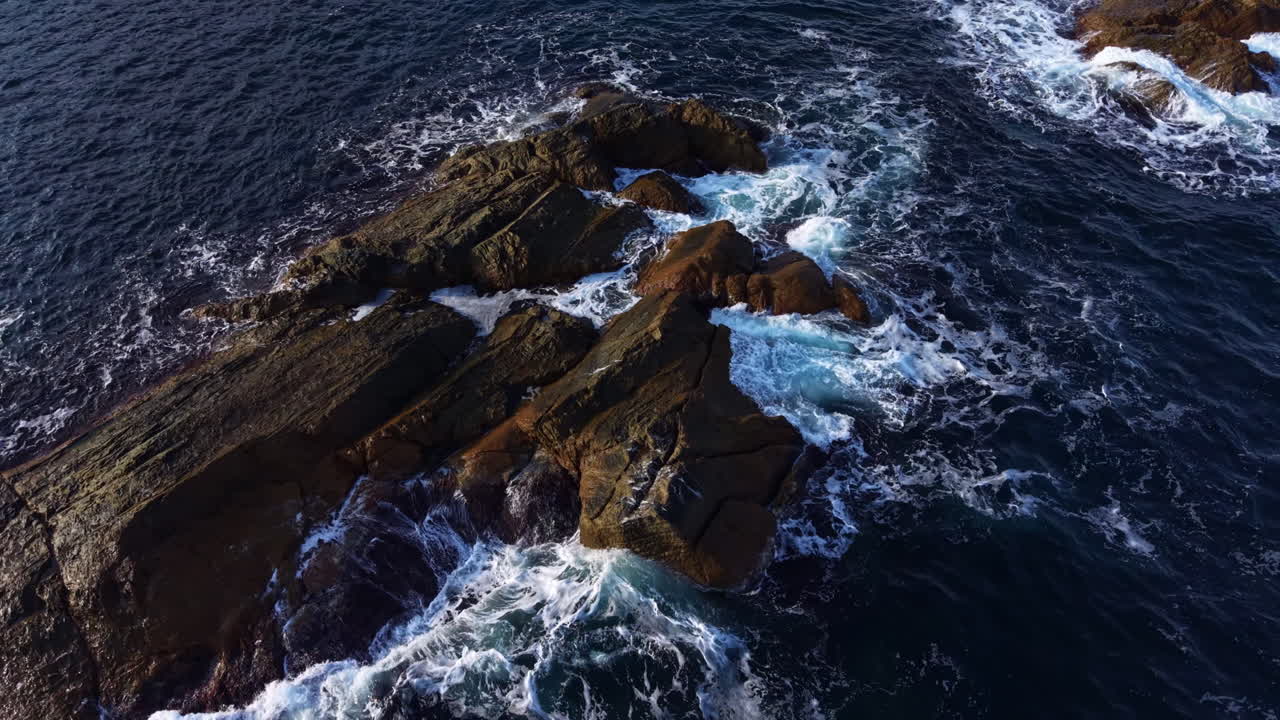 Le onde si infrangono contro rocce frastagliate lungo la serena costa sotto la luce solare splendente di mezzogiorno.