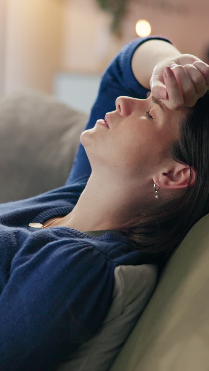 Una donna riposa su un divano, con un'espressione stanca e infelice