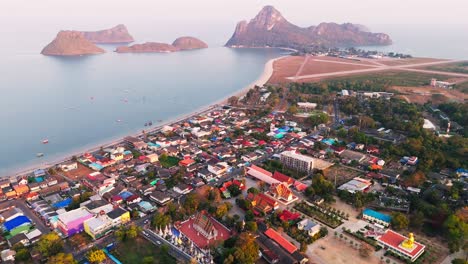 aerial descend over prachuap khiri khan thailand coastal city, oceanfront buildings, mountains, and stunning blue waters contrasting against vibrant gold red temples