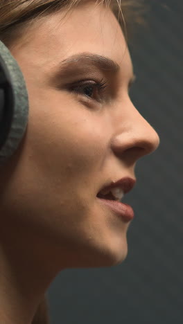 pretty happy young woman with large black headphones sings popular song with contemporary microphone in recording studio close side view